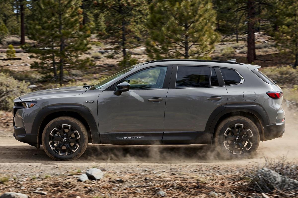 Mazda CX-50 Meridian Edition with all-terrain tires driving on a forest dirt trail.