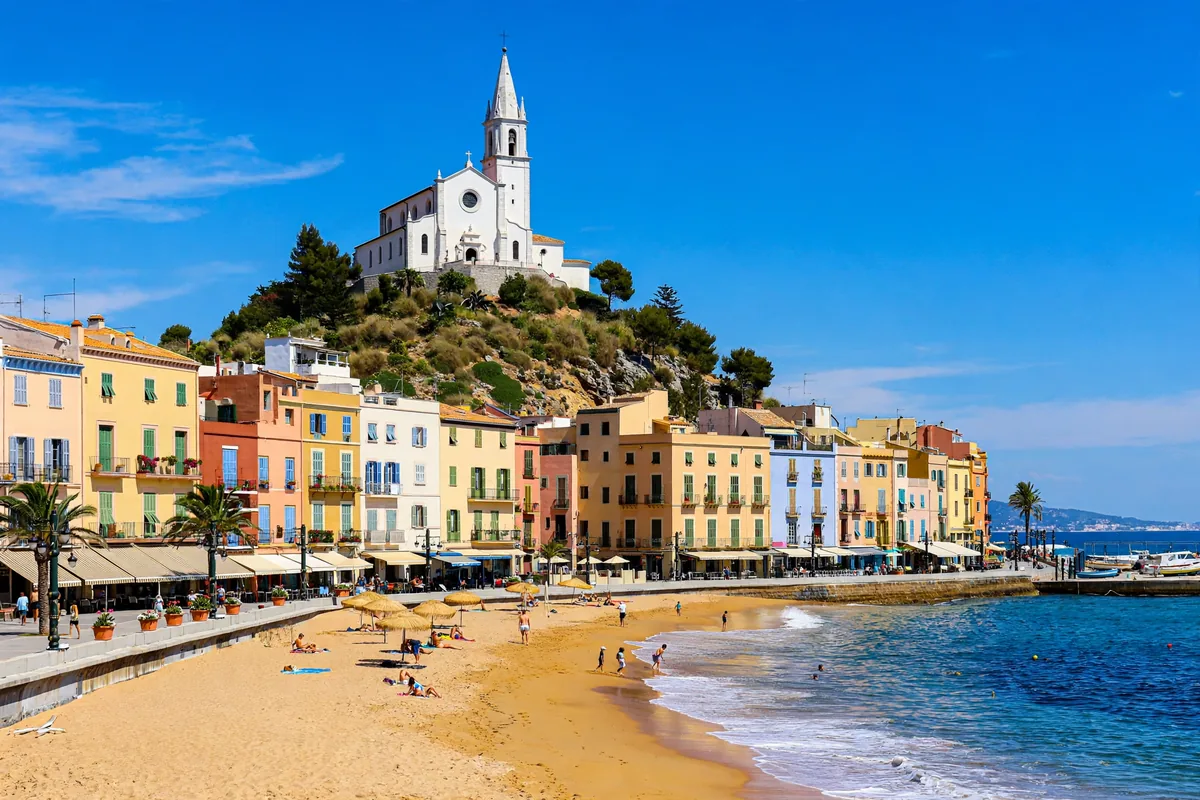 The Sitges seafront with the Sant Bartomeu church on a hill above golden sand and blue sea